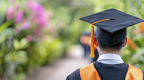 A back view of many students wearing black and orange graduation