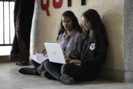 Two MBA students sitting and working on a laptop inside the campus of a top management college in Ahmedabad Gujarat, preparing for academic coursework.