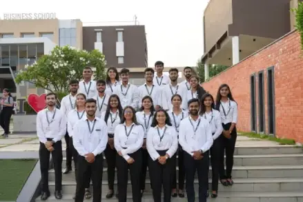Group of MBA students in formal attire posing on campus steps of a modern business school, representing professionalism and student culture.